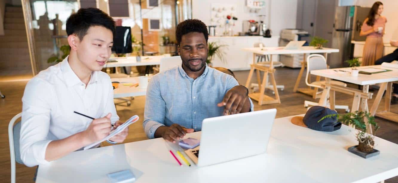 Two creative professionals sitting at desk looking at creative jobs in New Jersey on laptop